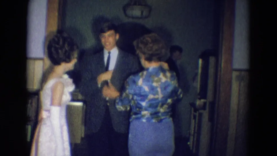 The white-dressed young woman and helper face a smiling suited man in the 1969 Diller, Nebraska home-movie scene.