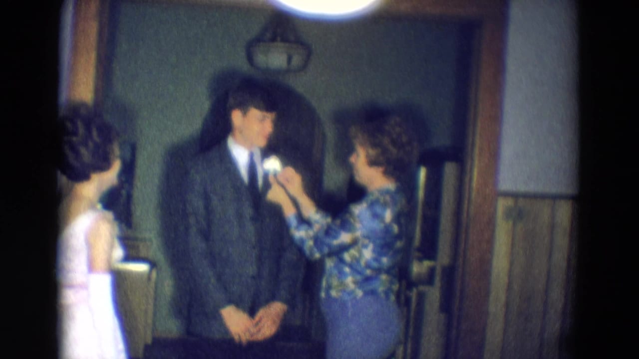Diller, Nebraska 1969 frame of a woman pinning a white flower to a young man's lapel in a dim wood-paneled hallway.