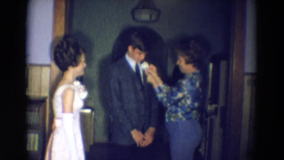 The final 1969 Diller, Nebraska frame shows three people indoors as a woman finishes pinning a boutonniere on a suited young man beside a young woman in white.