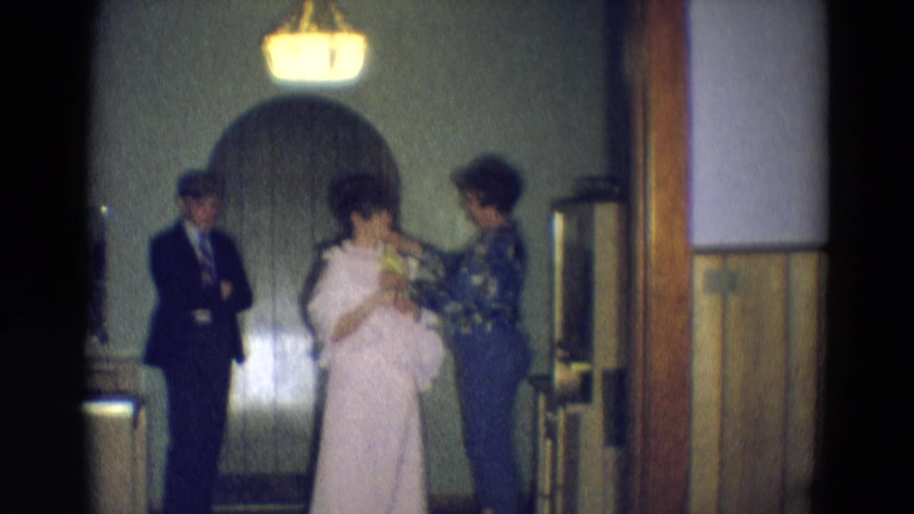 A woman in a light pink dress holds flowers as another adult helps her in a Diller, Nebraska interior during 1969 formal preparation.