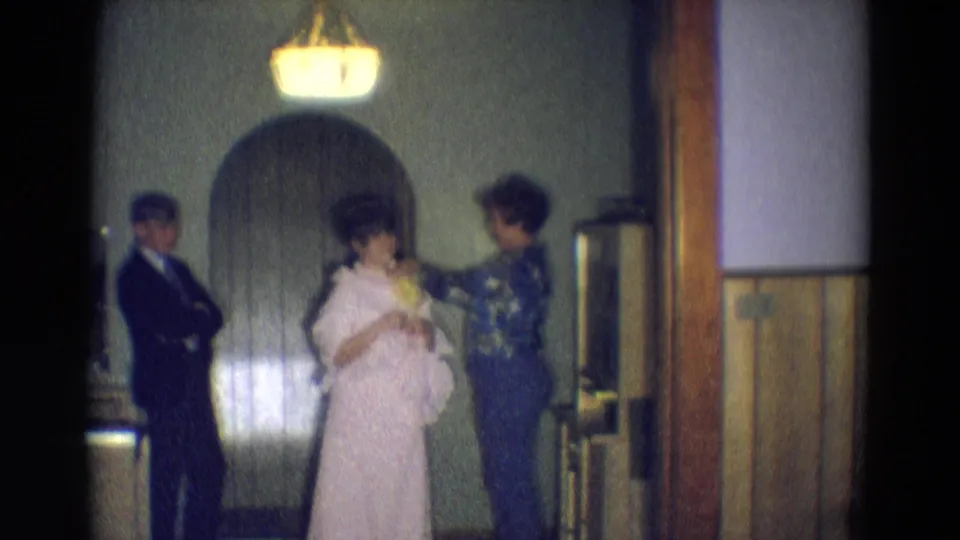In the 1969 Diller, Nebraska clip, a woman in a light pink dress stands in a hallway while another woman adjusts flowers or clothing.