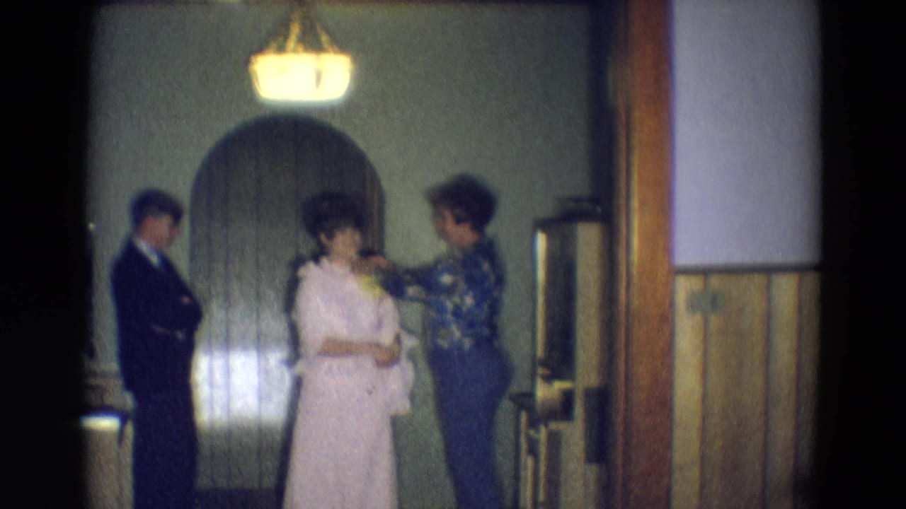 Two women stand near an arched doorway as a man in a dark suit waits at left.
