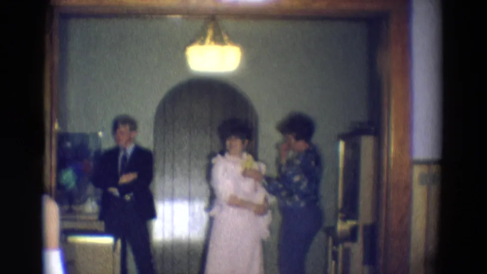 The woman in the pale gown turns more toward the camera while another woman stands close, with the suited man still waiting at left.