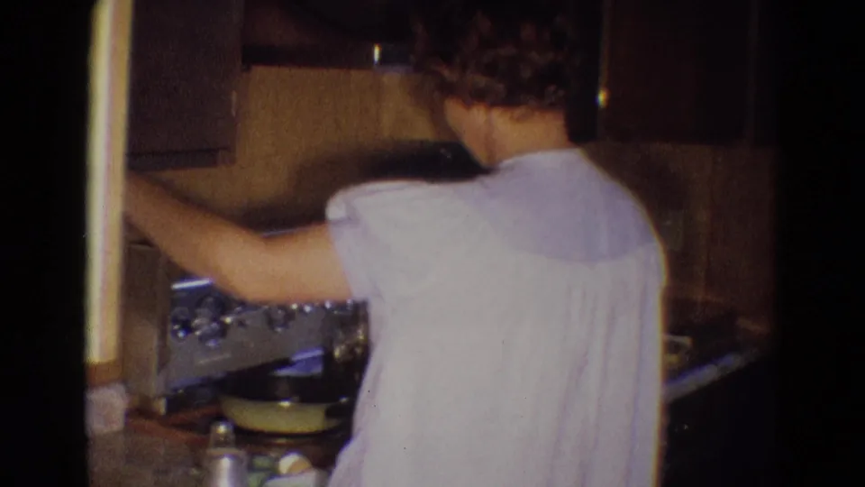The woman turns toward the stove, with her back partly to the camera, inside the 1969 Diller kitchen interior.
