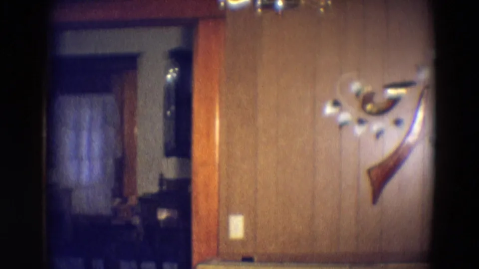 1969 Diller, Nebraska frame showing wood paneling, decorative wall ornament, light switch, and a doorway into a dim curtained room.
