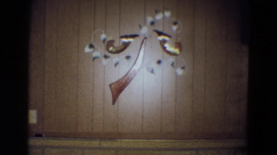 1969 Diller, Nebraska interior frame centering the abstract wall sculpture on wood paneling, with the ceiling light partly visible above.