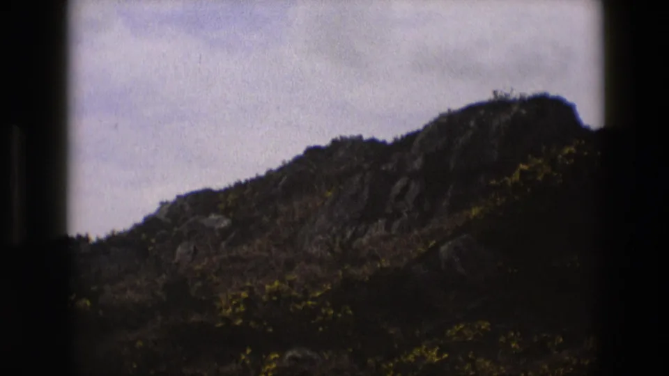 1969 England roadside view of a rugged hillside, framed by dark 8mm gate edges and muted color.