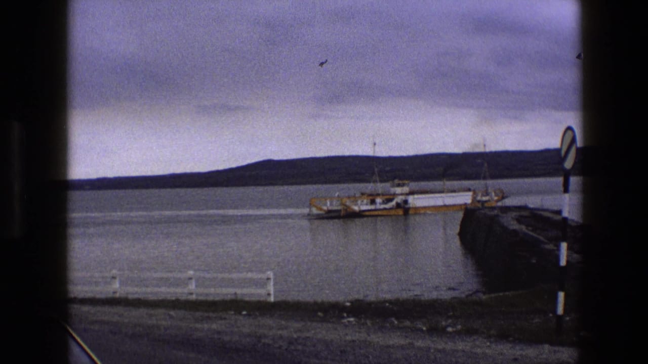 Ferry at a waterside pier with distant hills and dark clouds across the bay.