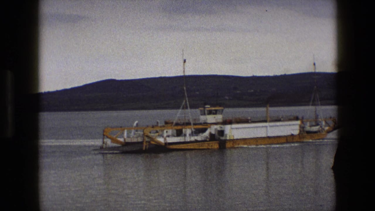 Small yellow-and-white ferry crossing calm water with a dark hillside behind it.