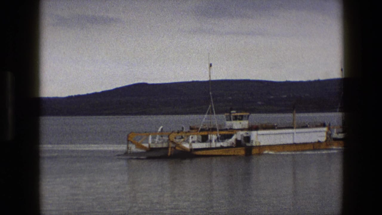 Yellow ferry continues across the water, framed by dark film borders and distant hills.