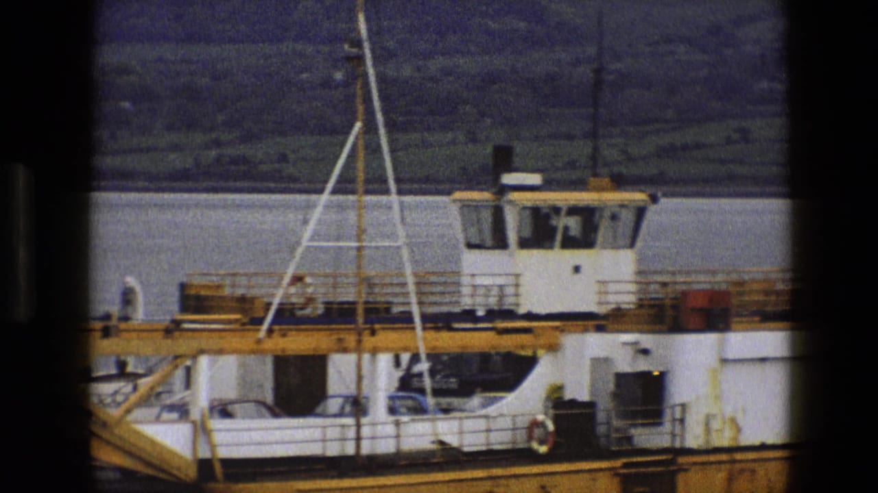 Ferry side and cabin beside water, with cars and a vessel marking partly visible.
