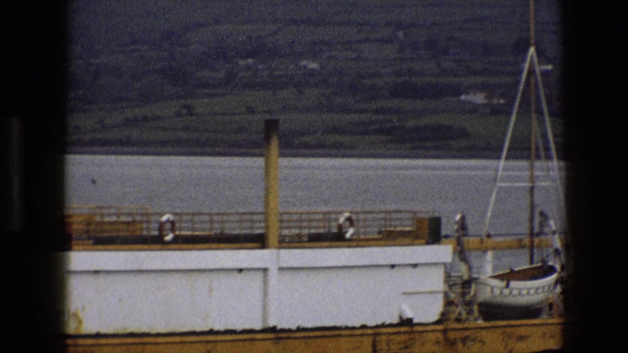 Large vessel seen through a dark frame on calm water with green hills behind it.