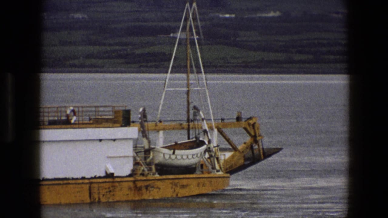 A closer 1969 England home-movie view of the vessel's stern area, with a secured lifeboat, railings, and calm water behind it.
