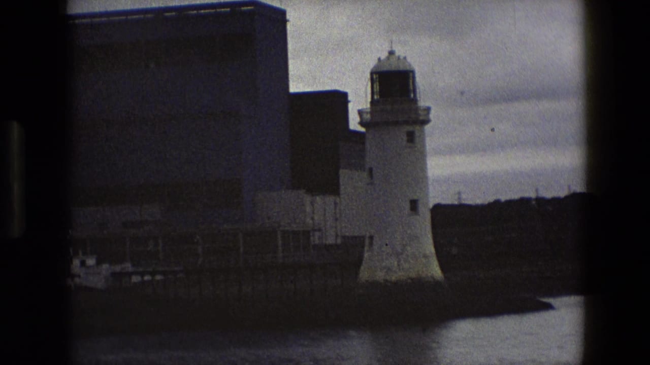 Closer view of white lighthouse beside a large waterfront industrial building.