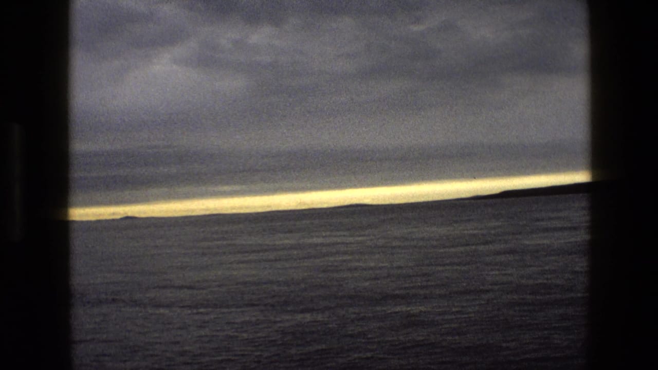 Dark-framed view across calm water toward a low horizon under heavy clouds at dusk.