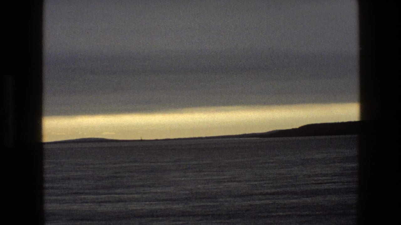 Twilight view over calm water and distant hills seen through dark window bars.
