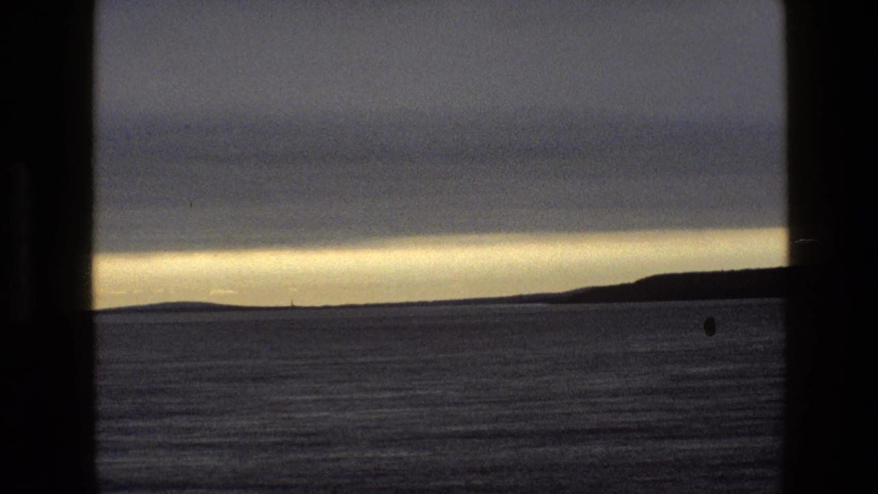 Cloudy twilight shoreline and water viewed through a window frame.