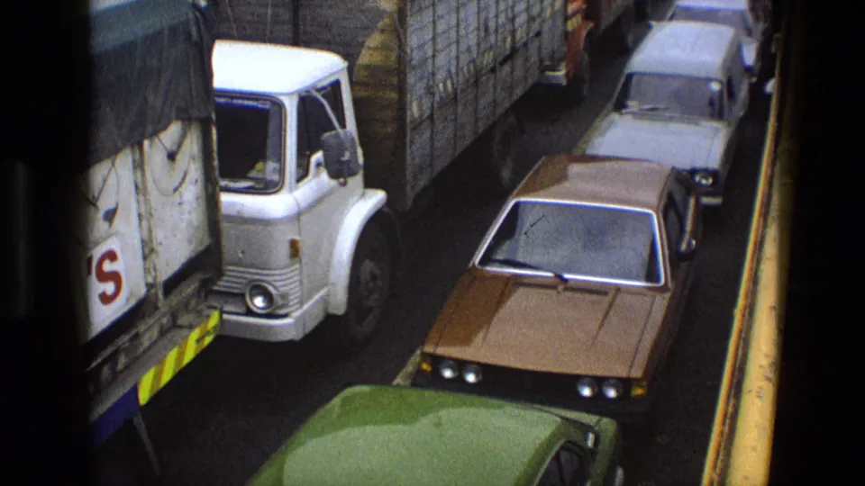 1969 England road congestion seen from above, with a covered lorry and classic cars compressed in a narrow lane.