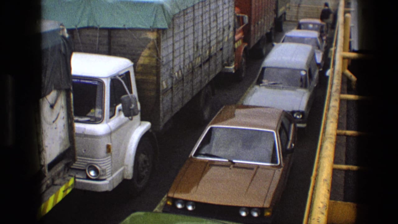 Cars and a white truck lined up on a ferry deck beside yellow railings.