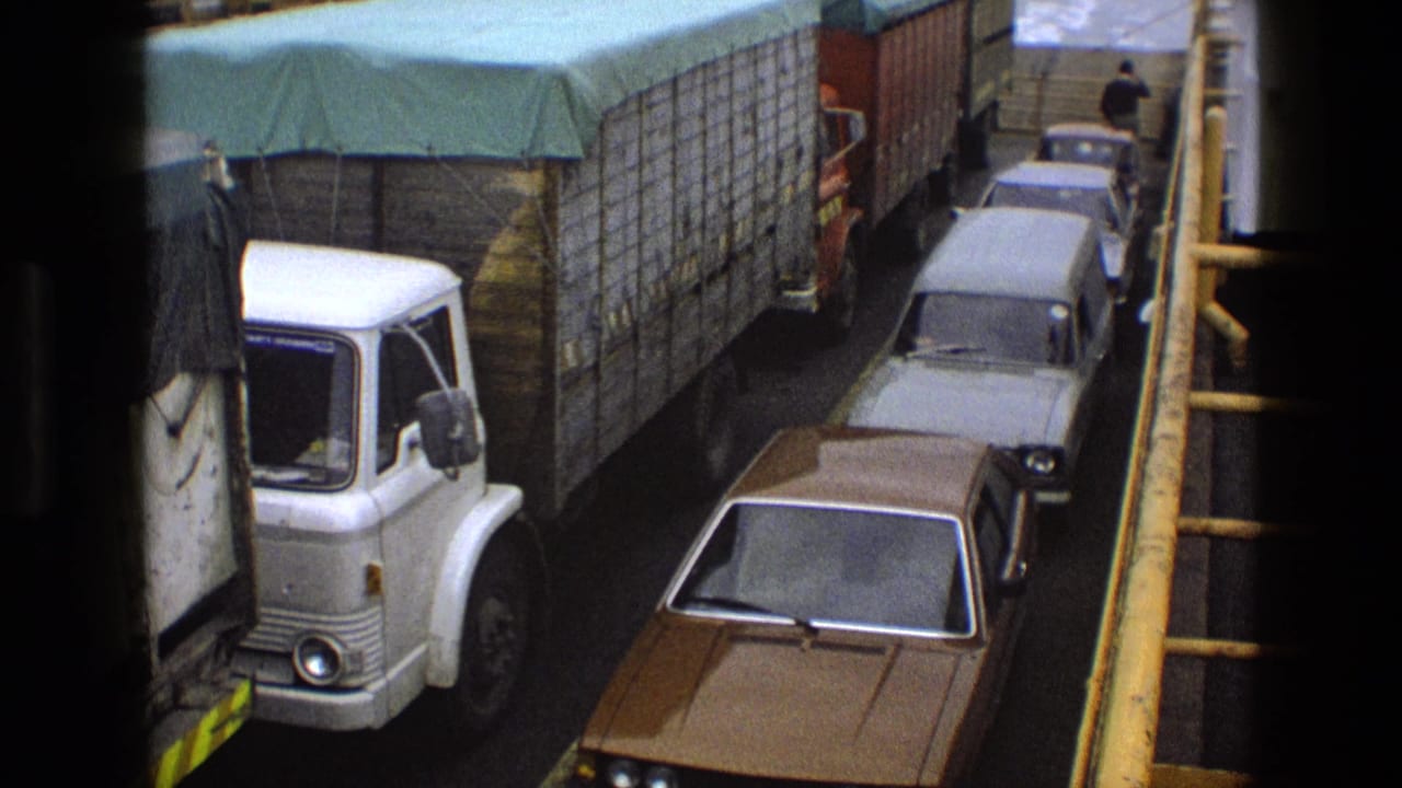 Line of vehicles on a ferry deck with a person visible near the far end.