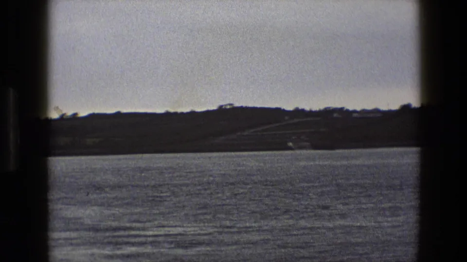 A quiet 1969 England waterside view shows rippled water, distant land, and dark 8mm frame borders.