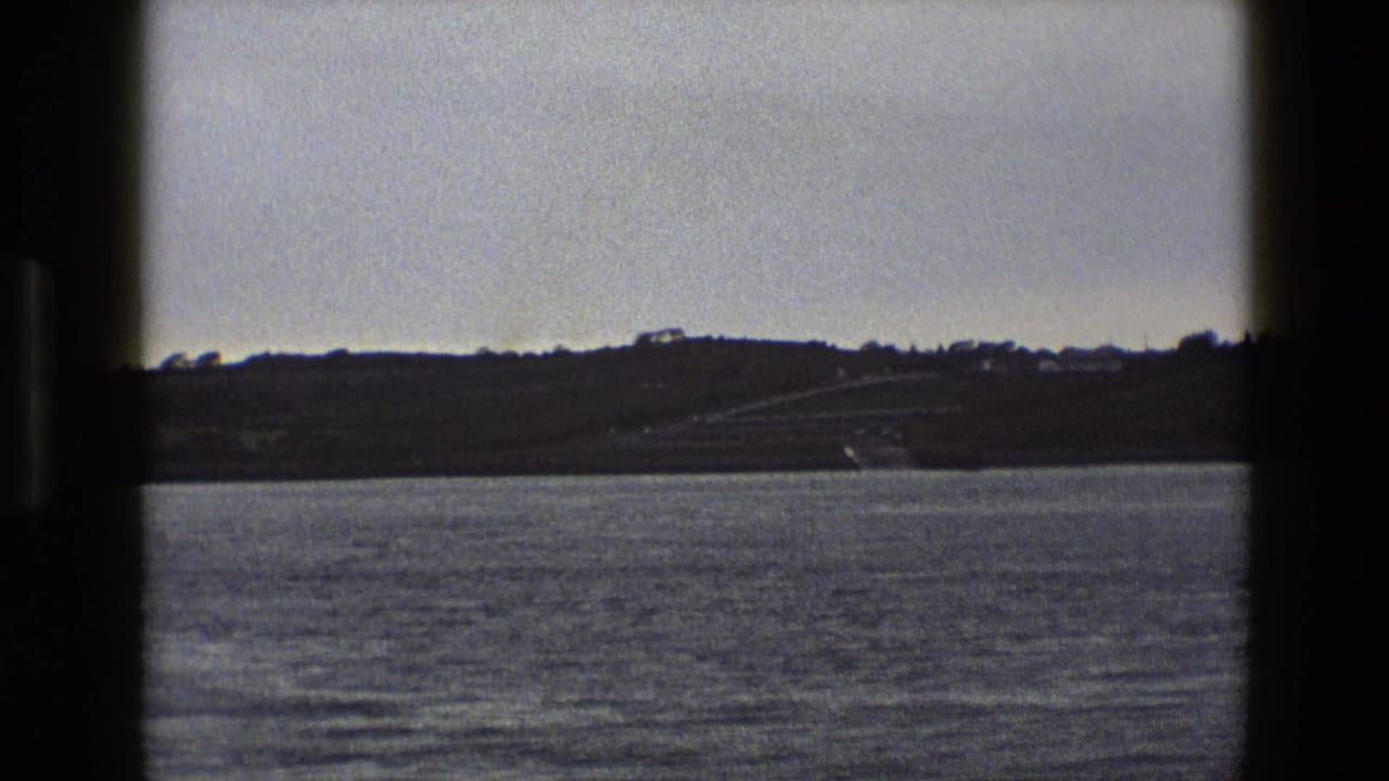Water in the foreground with a distant low hillside and scattered buildings beyond.