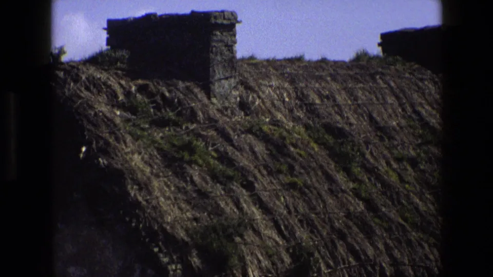 Close 1969 England home-movie view of the cottage roof, showing thick thatch and a rough stone chimney.