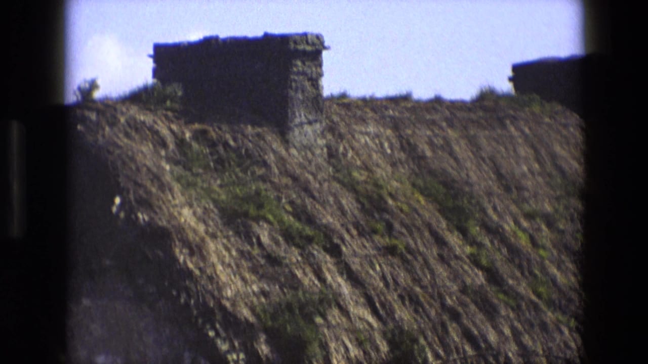 1969 England 8mm frame showing a close view of a thatched roof with a stone chimney and dark film borders.