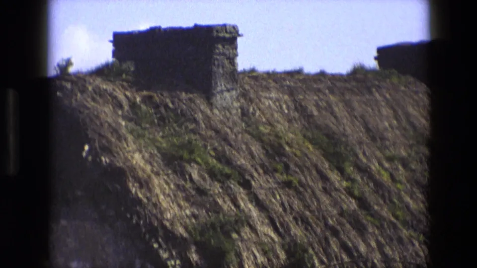 1969 England 8mm frame showing a close view of a thatched roof with a stone chimney and dark film borders.
