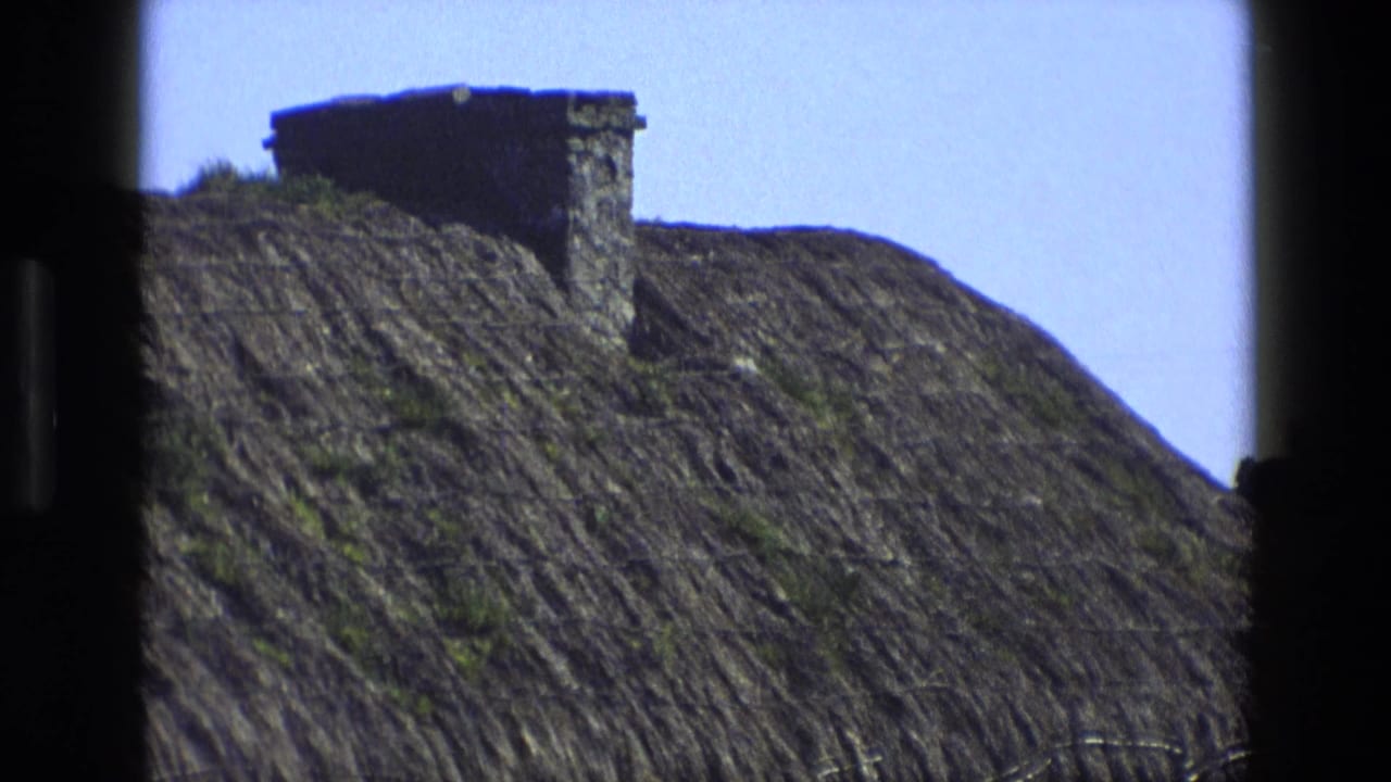 Close exterior view of a rural English thatched roof with a stone chimney, recorded on 8mm film in 1969.
