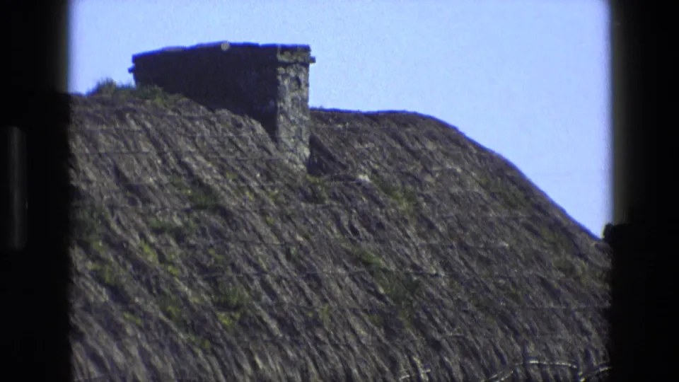 Close exterior view of a rural English thatched roof with a stone chimney, recorded on 8mm film in 1969.