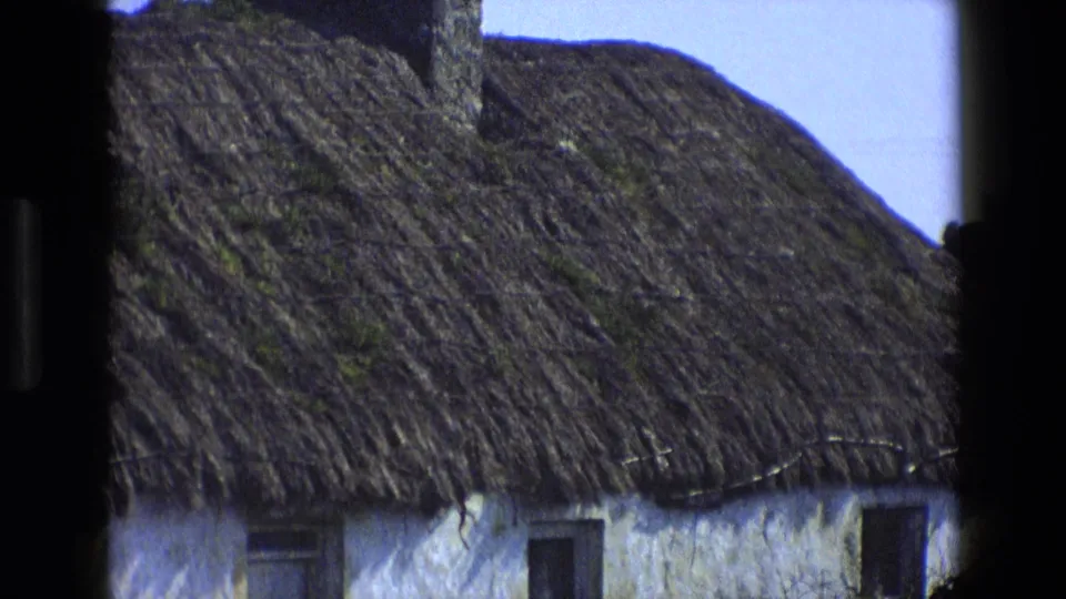 1969 England frame showing the lower thatched roof edge over a whitewashed cottage wall with dark windows.