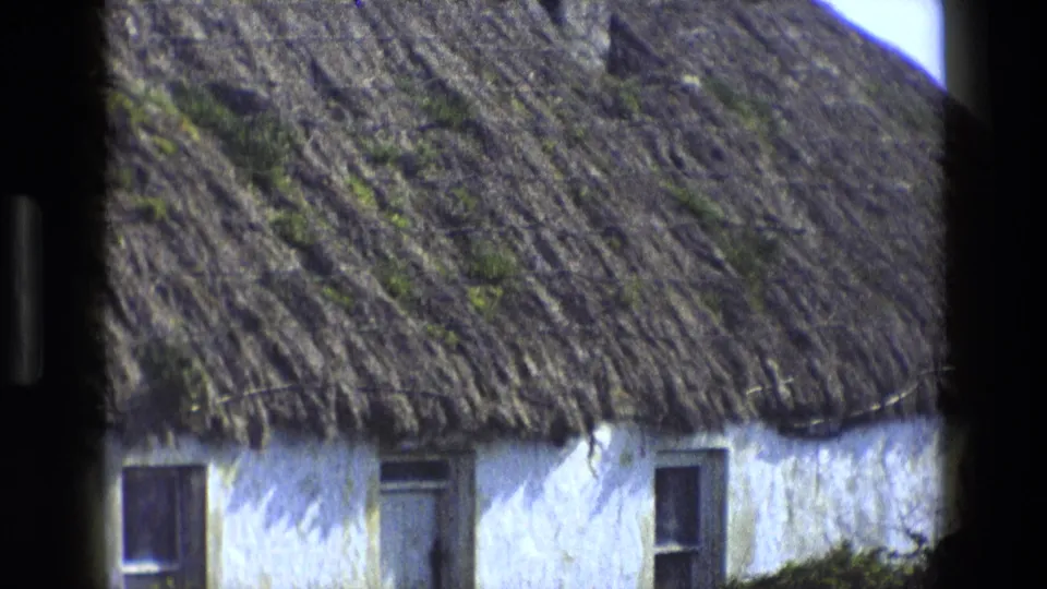 The frame settles on the cottage wall, roof eaves, windows, and weathered thatch in rural England footage from 1969.