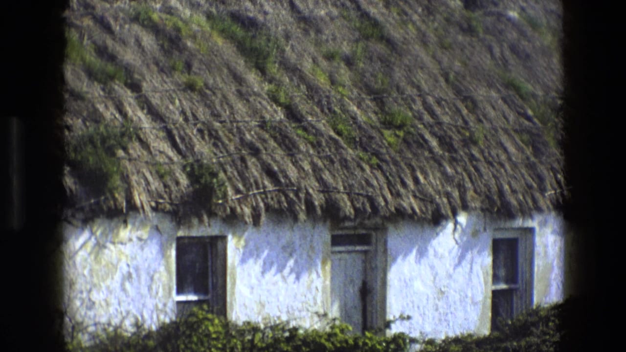 Whitewashed thatched cottage seen through dark vertical frame edges.
