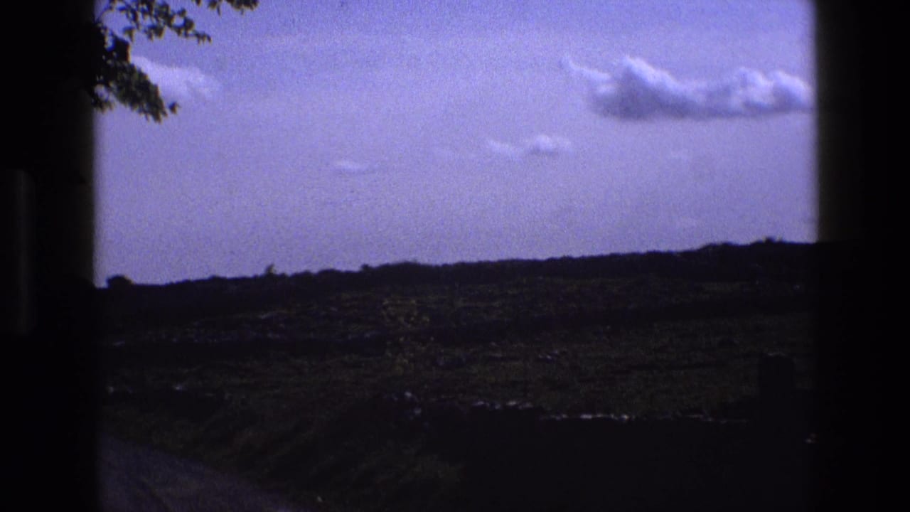 Rural fields under a pale blue sky, seen through dark vehicle or window framing.