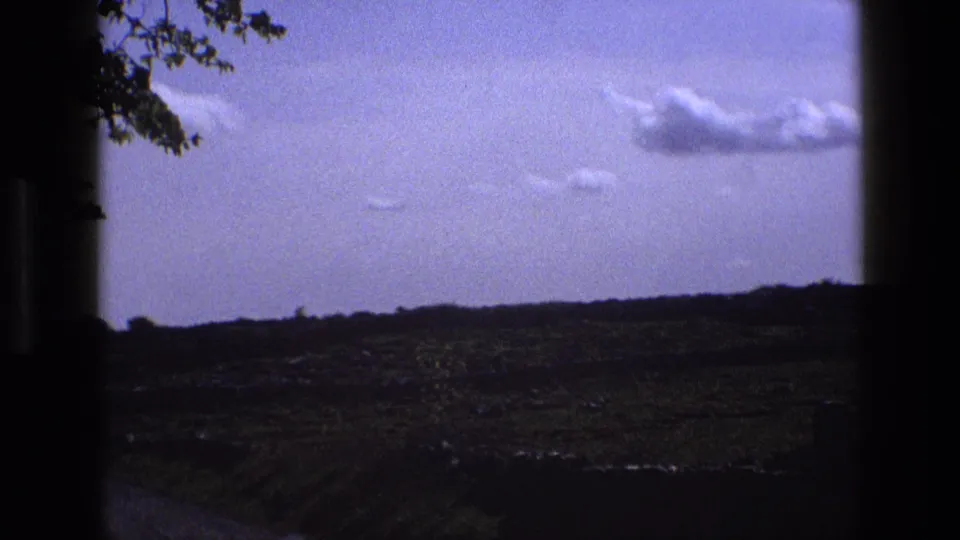 1969 England rural landscape with a broad sky, low fields, and dark side borders suggesting a moving window view.