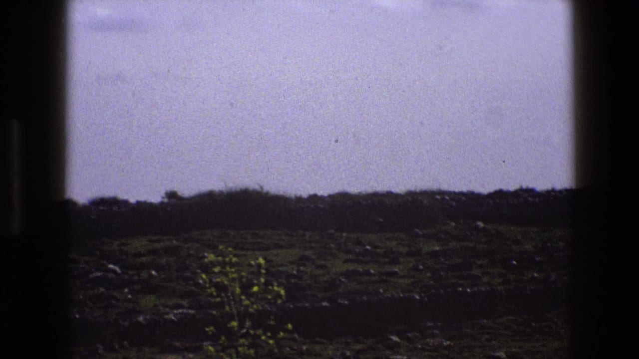 Rocky grass field seen through dark window-frame edges under a pale sky.