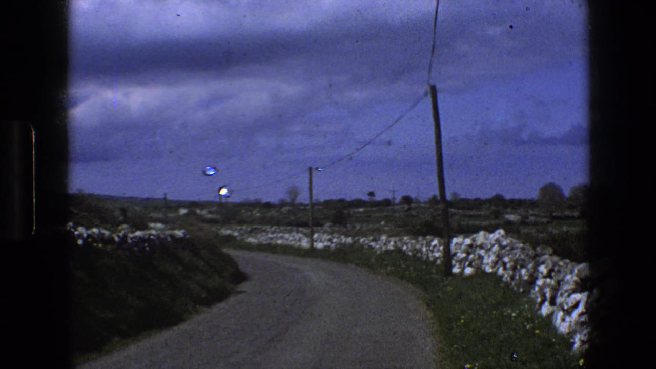 1969 England rural road curving through open fields with dry-stone walls, utility poles, and an overcast sky.
