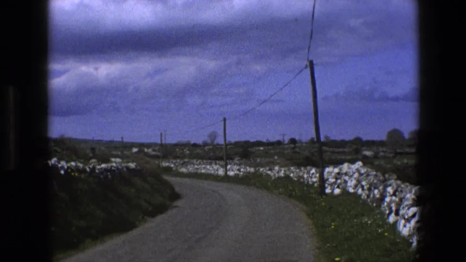 1969 England home-movie view of a curving country lane bordered by stone walls and grassy verges.