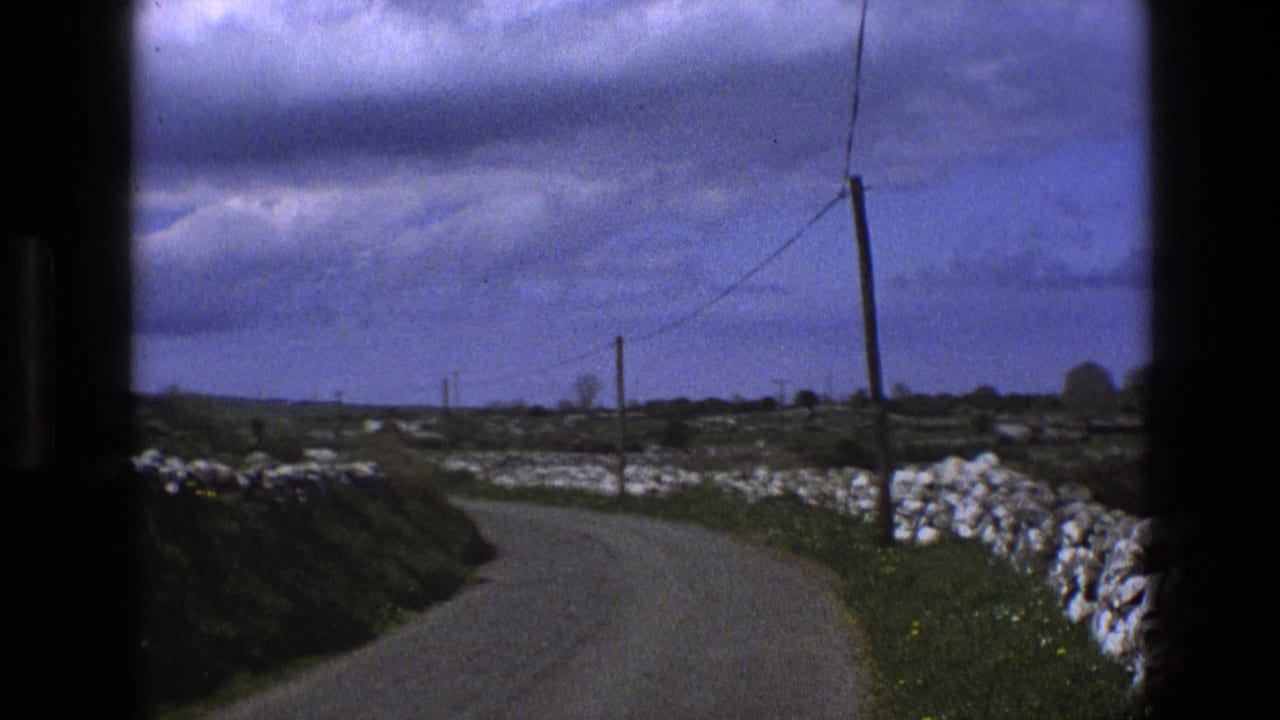 1969 England 8mm view from a moving vehicle on a curving country road with white stone walls, fields, and telephone wires.