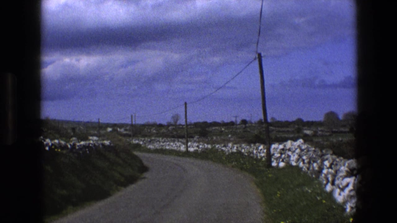 Rural lane curves past stone walls, fields, telephone poles, and overhead wires.