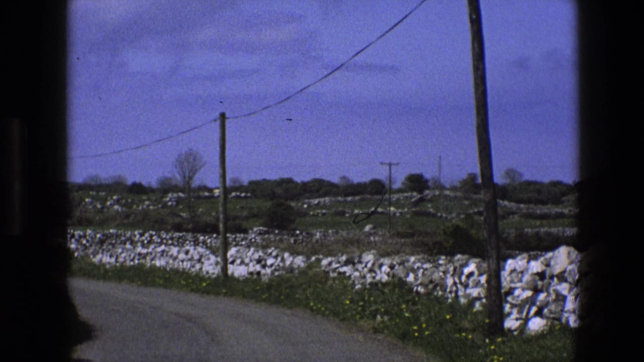 1969 England rural roadside view from a moving vehicle, showing dry-stone walls, fields, wooden power poles, and overhead wires.