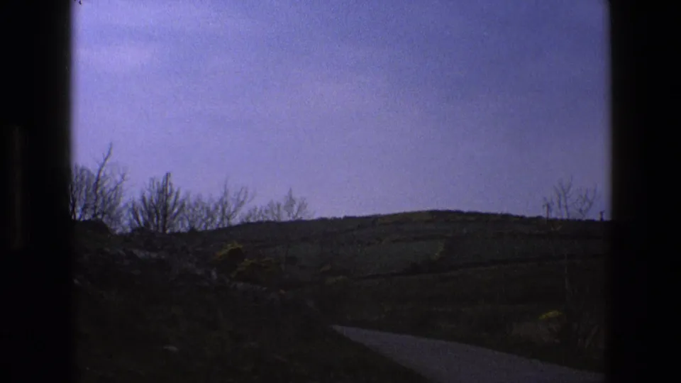 A dim English countryside view shows a hillside, low vegetation, and a narrow road or lane, with no sheep visible in this final 1969 frame.