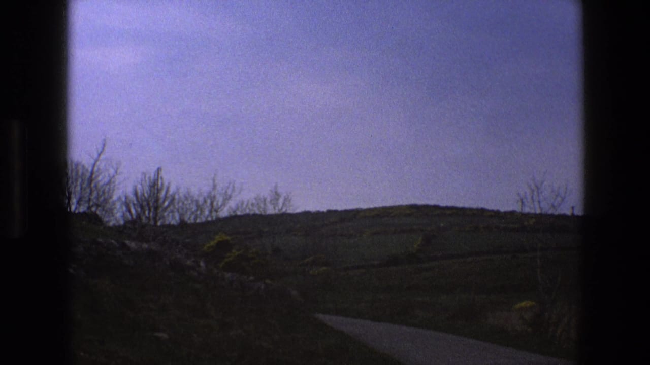 Rural road and rolling hills seen through a dark window edge with no car visible.