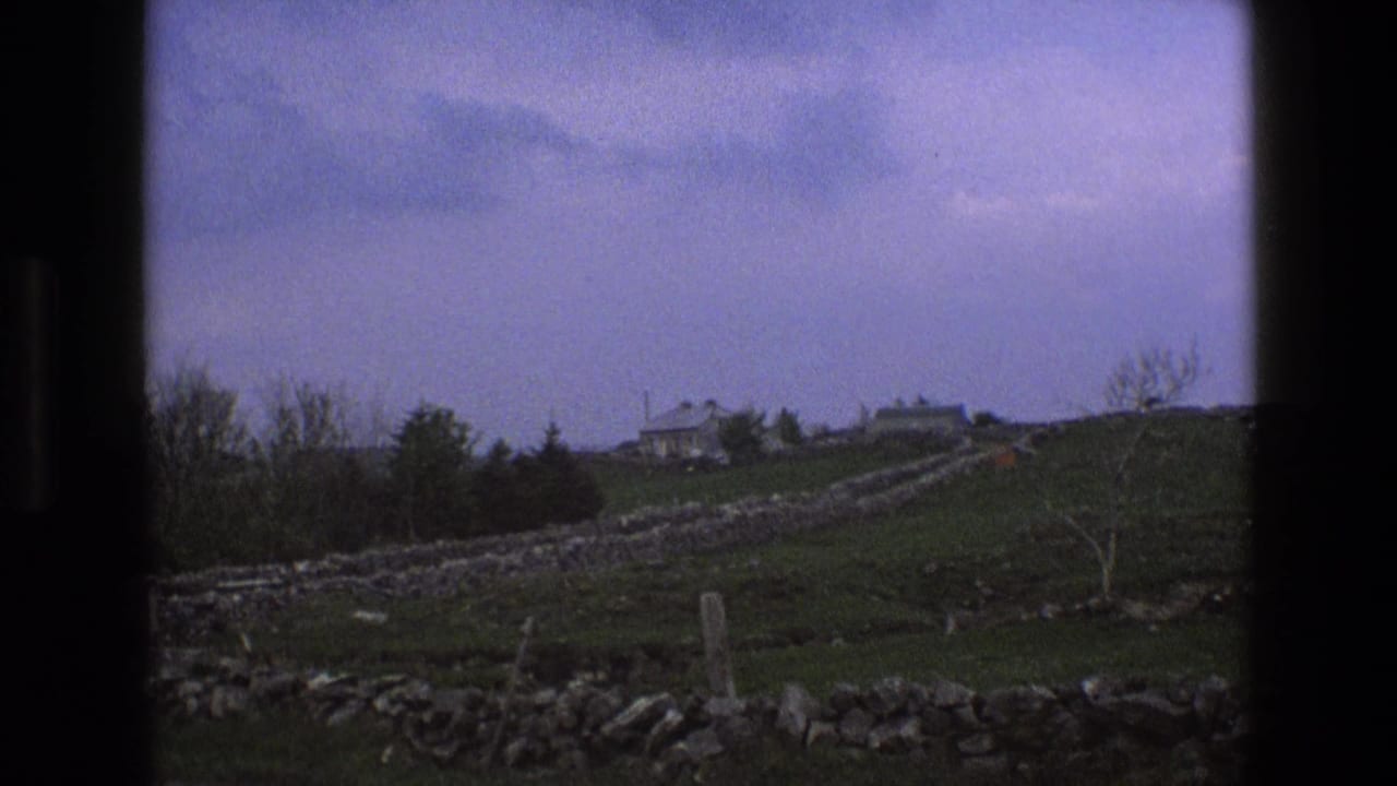 Rolling green fields with stone walls leading toward farmhouse buildings on a ridge.