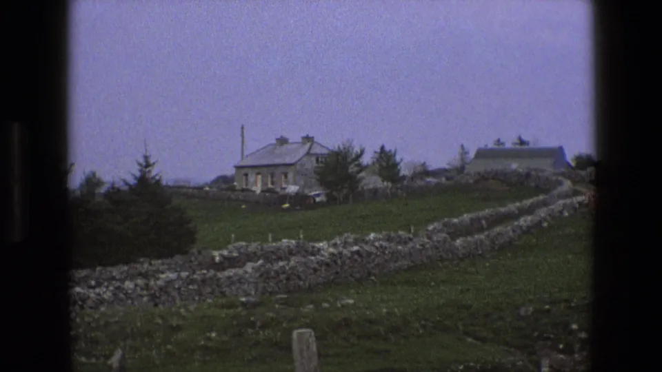 1969 England 8mm still with a closer view of a stone farmhouse, nearby trees, green fields, and stacked stone boundary walls.