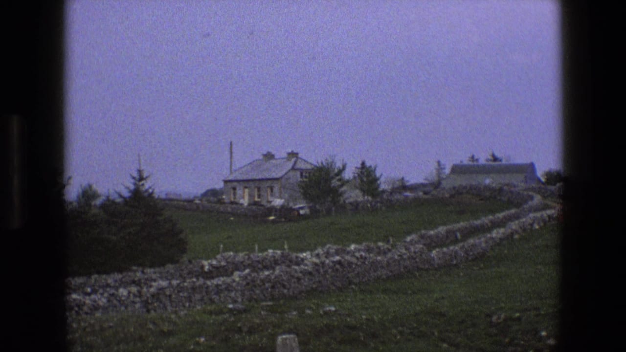 1969 England 8mm frame showing a stone cottage, gray roof, pasture, and dry-stone walls viewed through dark frame edges.