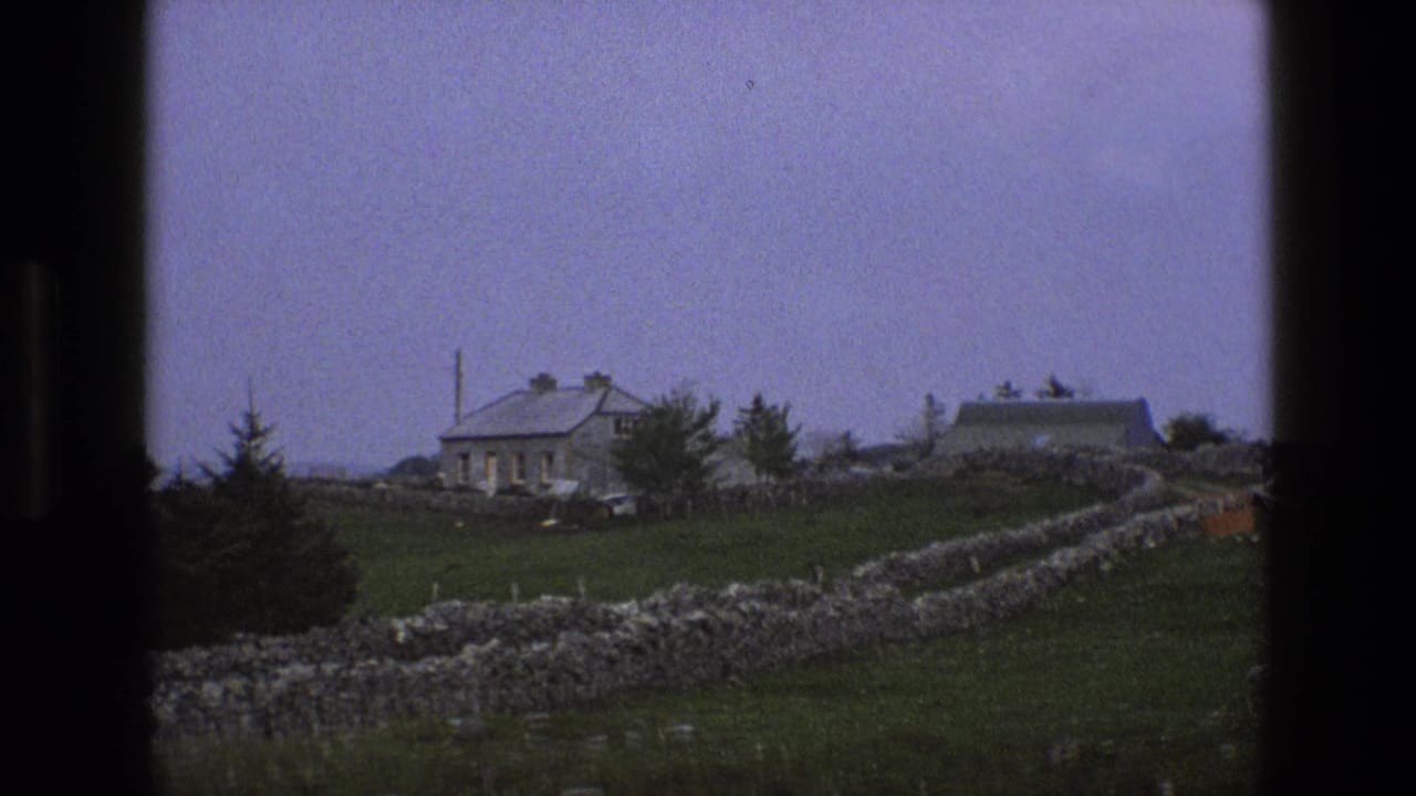 Rural stone buildings behind dry-stone walls and green pasture.