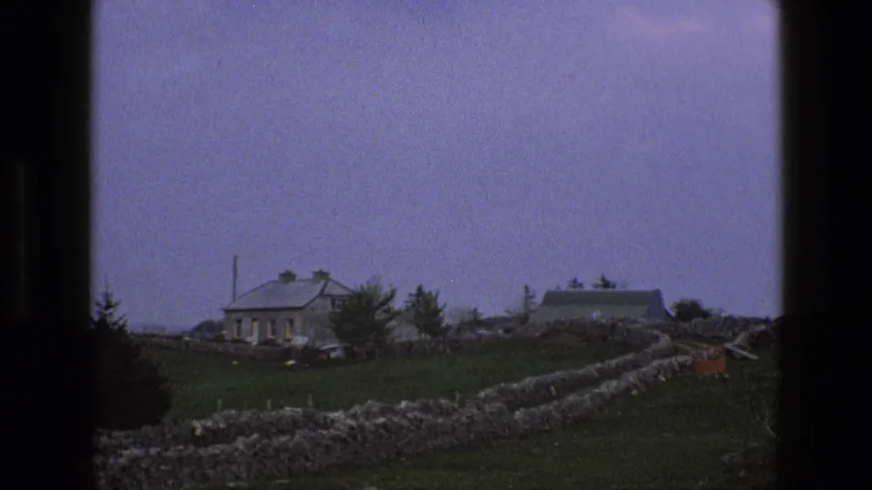 1969 England countryside frame with dry-stone walls, a stone cottage, adjacent farm building, trees, and open pasture.