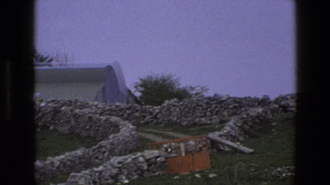 Stone walls and grass in front of a pale curved-roof building with an orange barrier nearby.